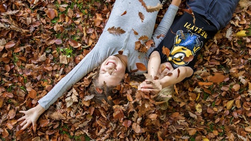 Two children lying down in a pile of autumn leaves laughing
